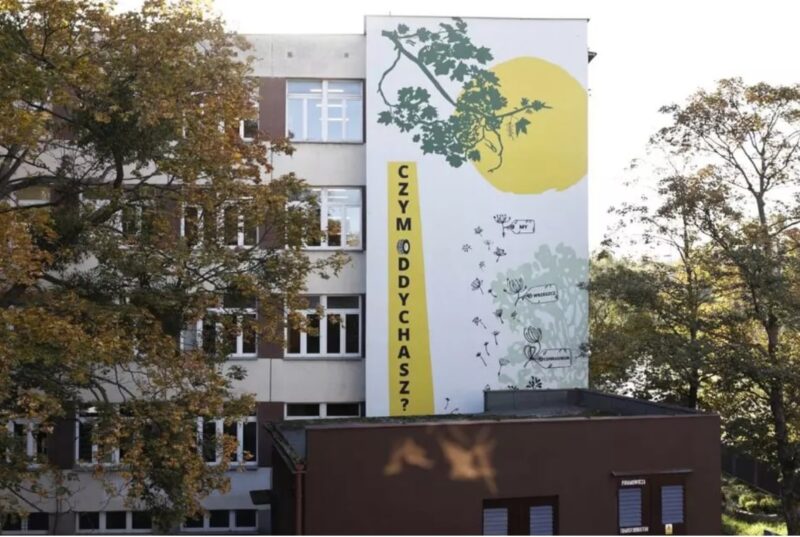Budynek piętrowy z muralem przedstawiającym żółty okrąg i nachodzące na niego gałęzie drzewa